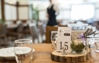 Una mesa de comedor con un mantel individual numerado, una vela en un tarro de vidrio y un centro de mesa de madera rústica.