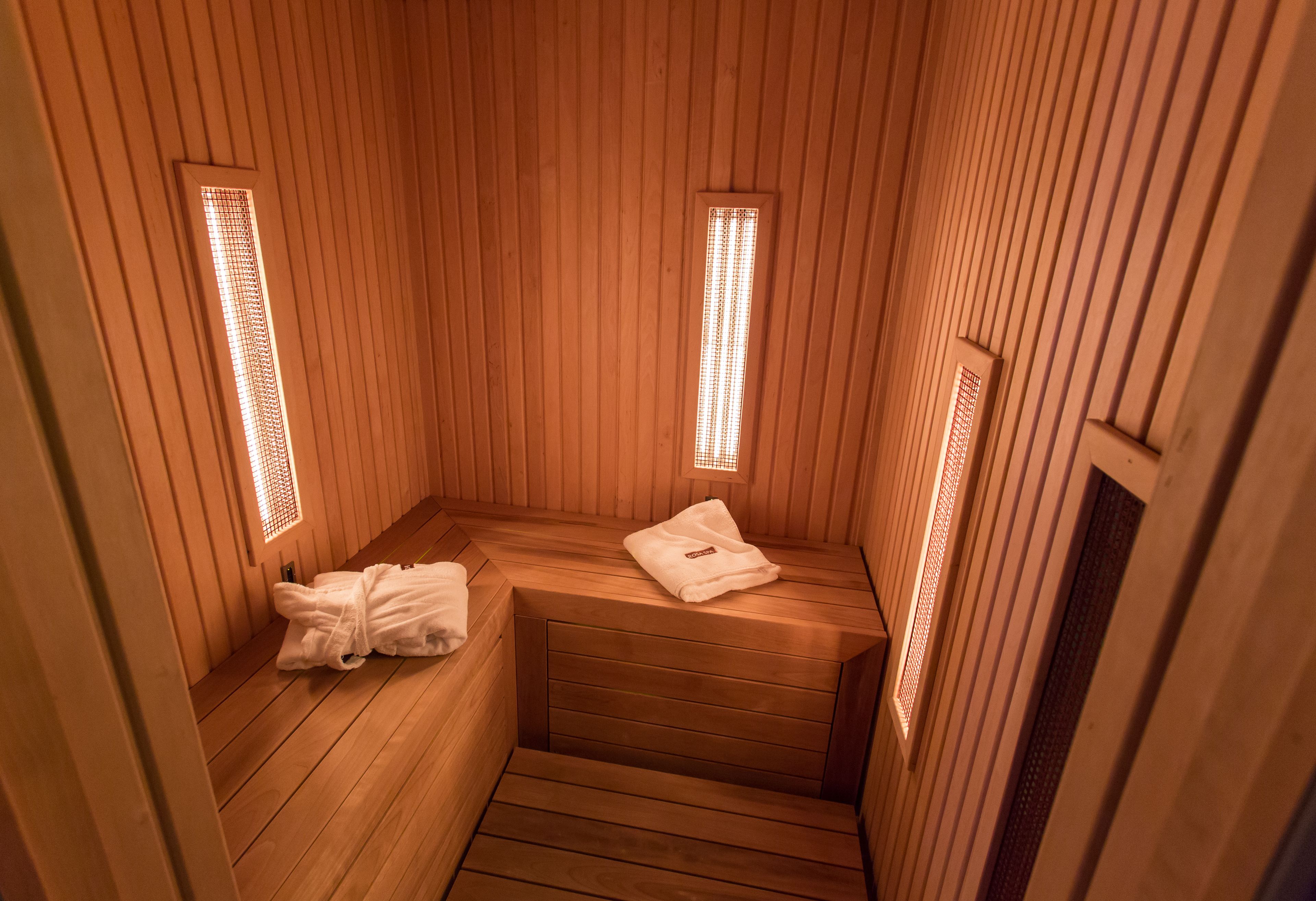 A sauna with wooden walls and benches, two small windows with light fixtures, and a towel on one bench.