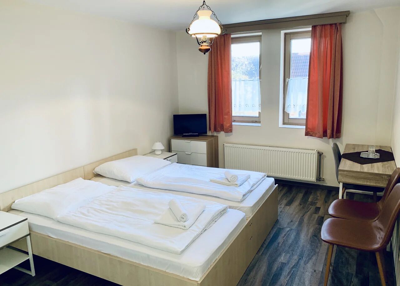Une chambre d’hôtel avec deux lits, un bureau, une chaise, une télévision et une fenêtre avec des rideaux.