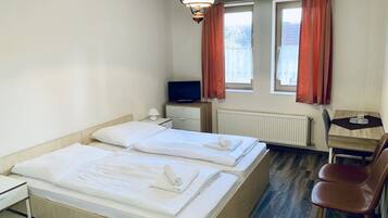 Une chambre d’hôtel avec deux lits, un bureau, une chaise, une télévision et une fenêtre avec des rideaux.