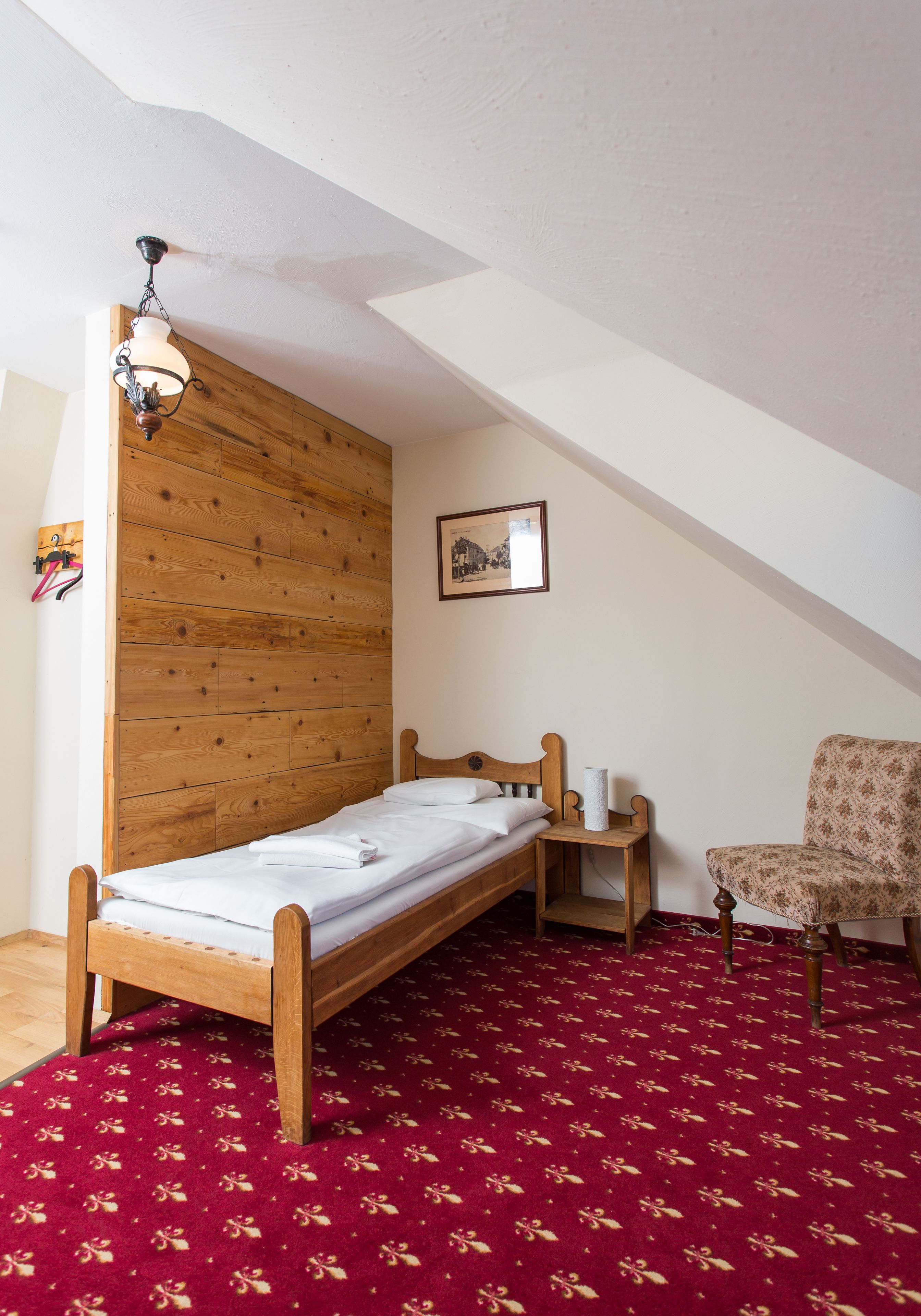 Una habitación pequeña y acogedora con una cama litera de madera, una mesita con una lámpara, una silla y una alfombra roja estampada.