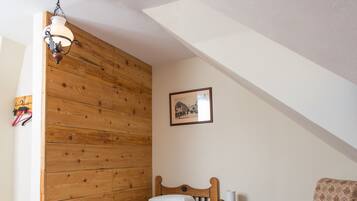 Una habitación pequeña y acogedora con una cama litera de madera, una mesita con una lámpara, una silla y una alfombra roja estampada.