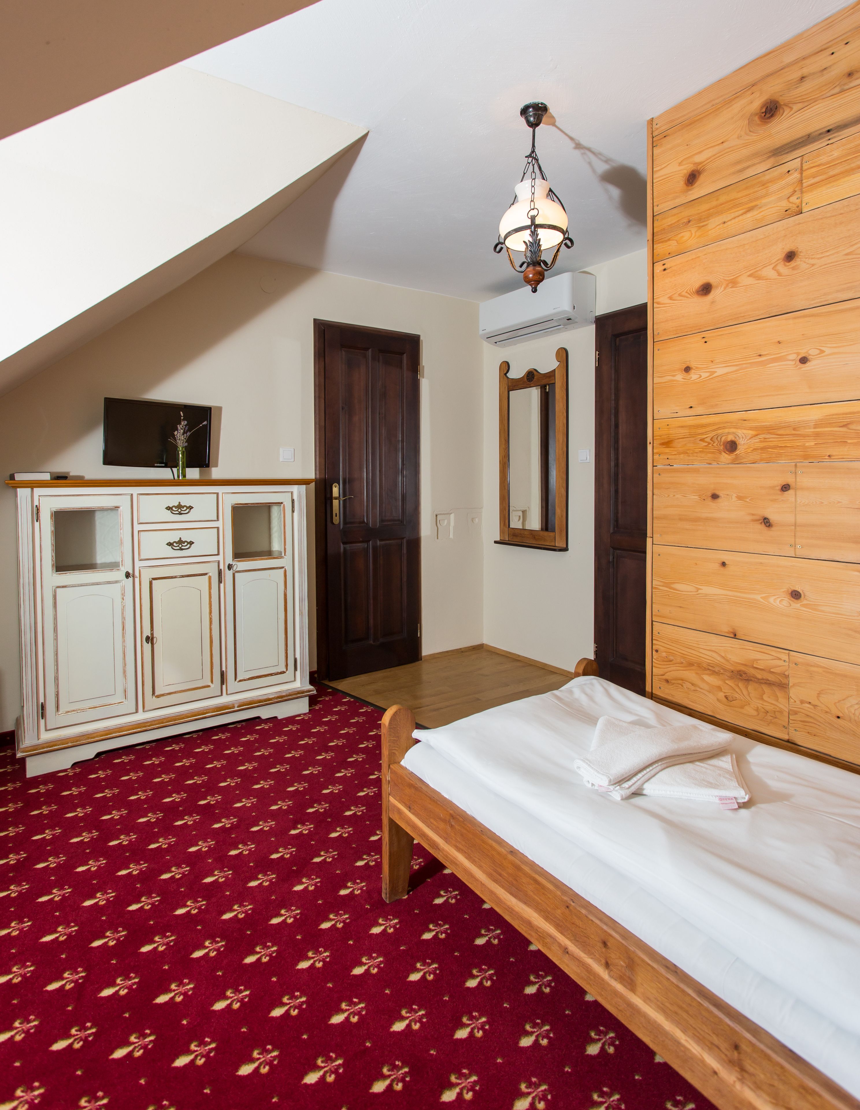 Una camera da letto con un letto in legno, una cassettiera bianca, un armadio in legno, uno specchio e un lampadario.