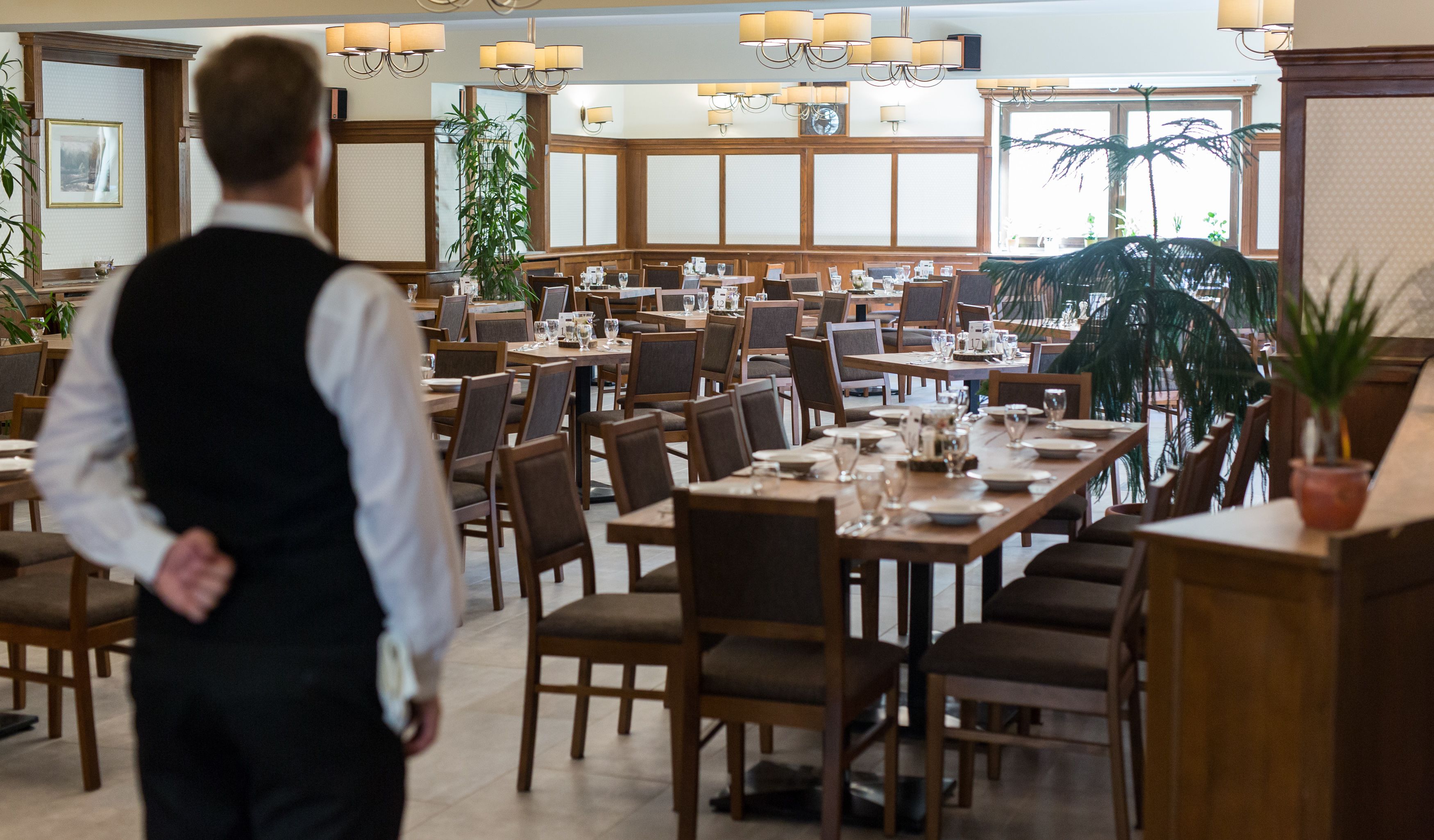 Un vaste espace dédié à la salle à manger, avec de nombreuses tables et chaises, un lambris en bois et de grandes fenêtres qui laissent entrer la lumière naturelle.
