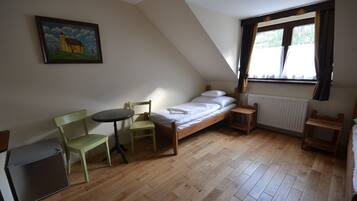 A small, cozy room with a bed, a chair, a table, and a radiator.