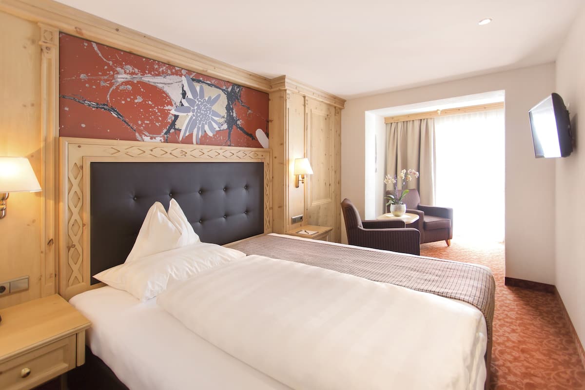 Habitación de hotel con una cama grande, escritorio, silla, televisor y ventana con cortinas.