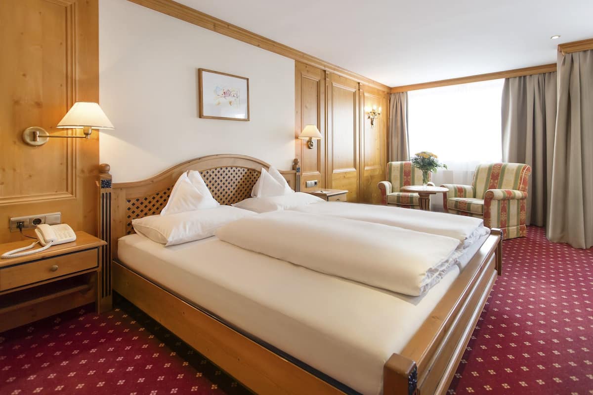 Habitación de hotel con cama doble, mesita de noche con lámpara, teléfono, pequeña mesa con silla y vistas al exterior a través de una ventana.