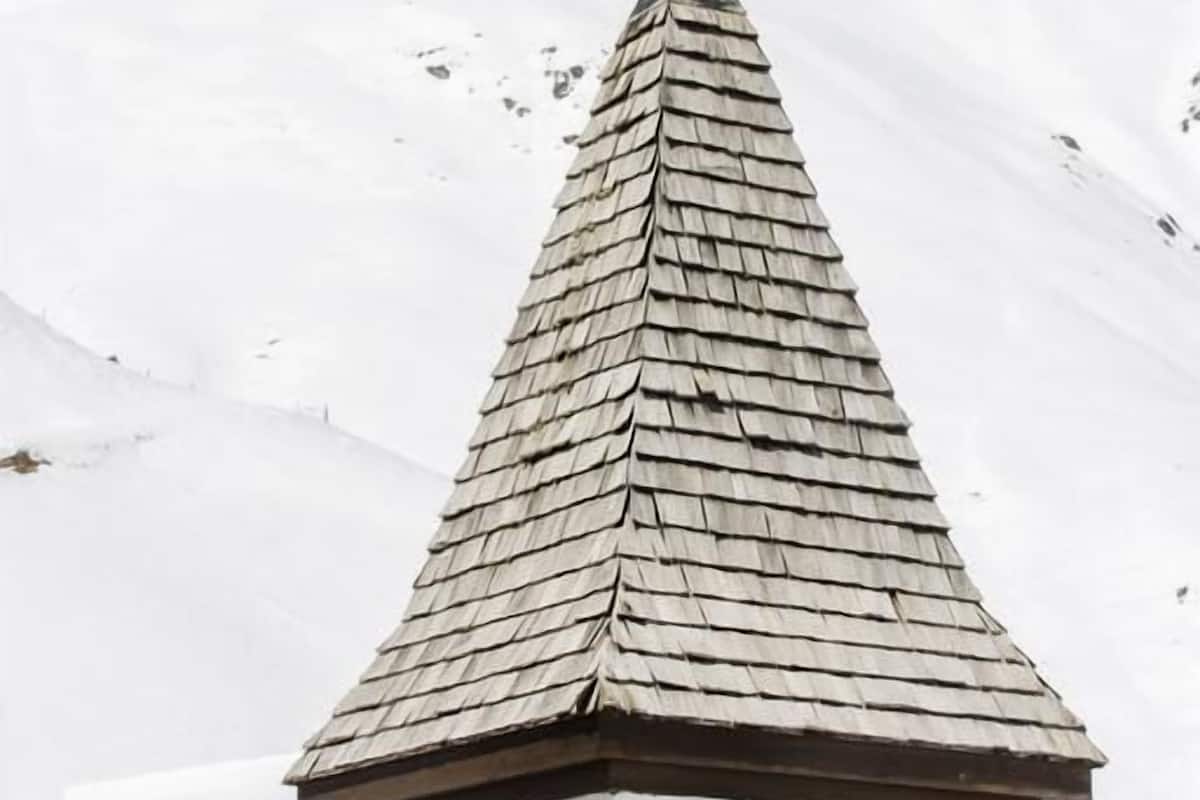 Una iglesia con un campanario puntiagudo coronado por una cruz dorada, con una imponente montaña nevada al fondo.