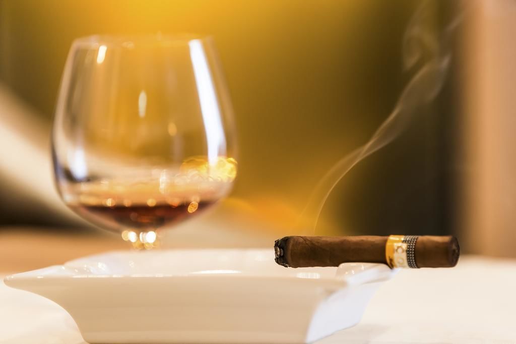 A glass of red wine and a cigar on a white plate.