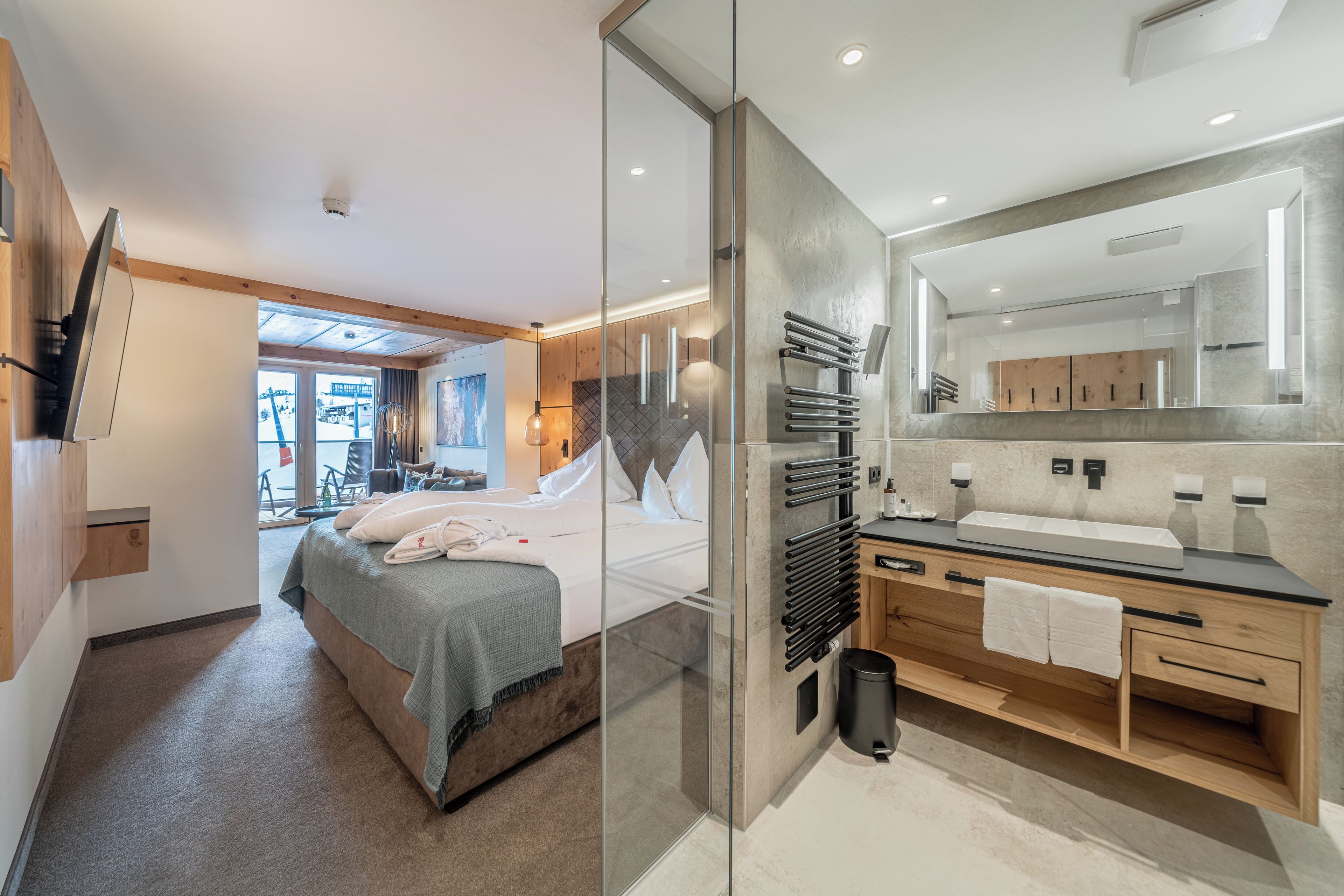 Ein modernes Hotelzimmer mit Bett, einer Glaskabine, einem Badezimmer mit Spiegel und Blick ins Freie.