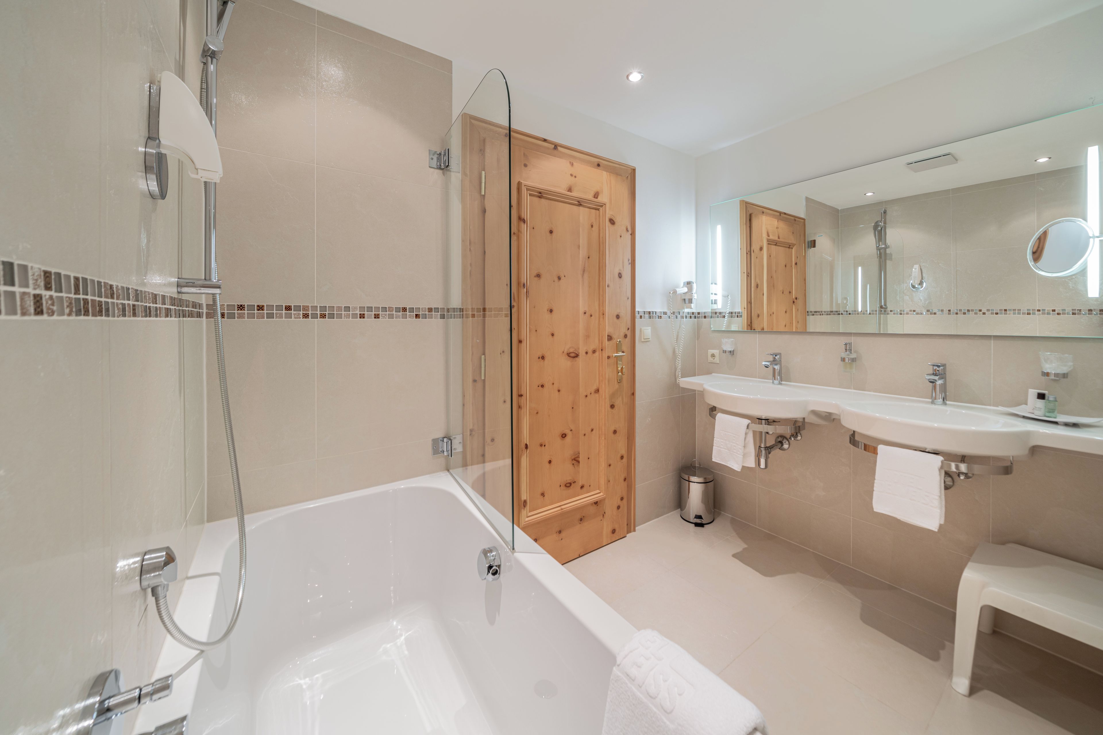 A modern bathroom with a bathtub, two sinks, a shower, and a wooden door.