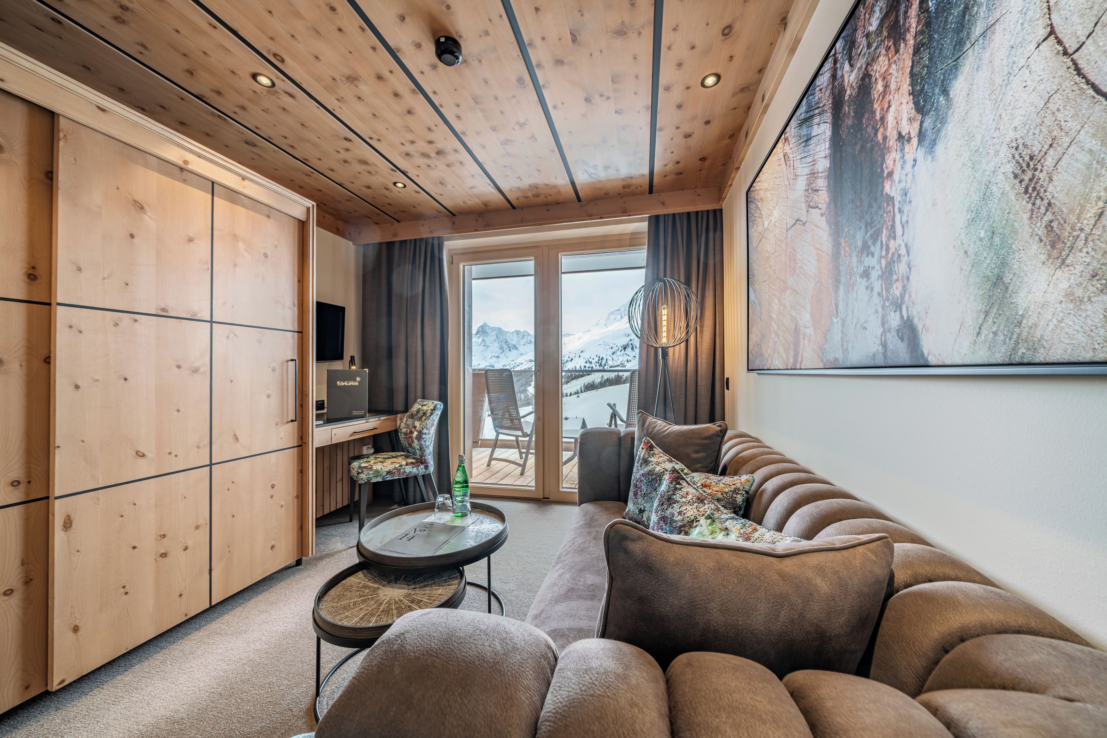 A modern interior with a wooden ceiling, a sofa set, a dining table, and a large window with a view of a snowy landscape.