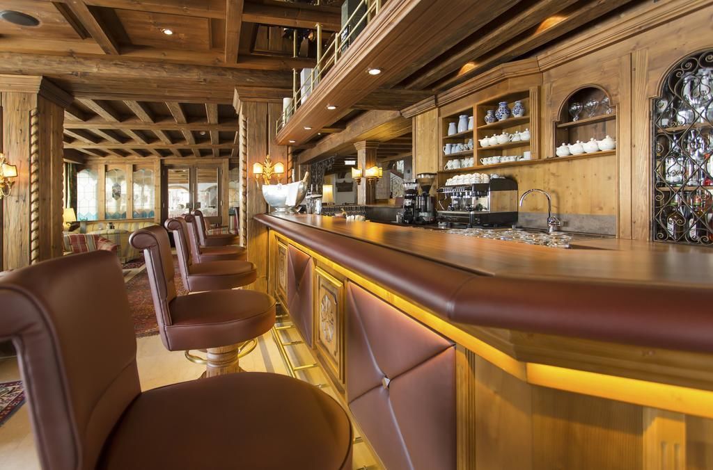 A bar area with wooden beams, leather barstools, and a counter with various items.