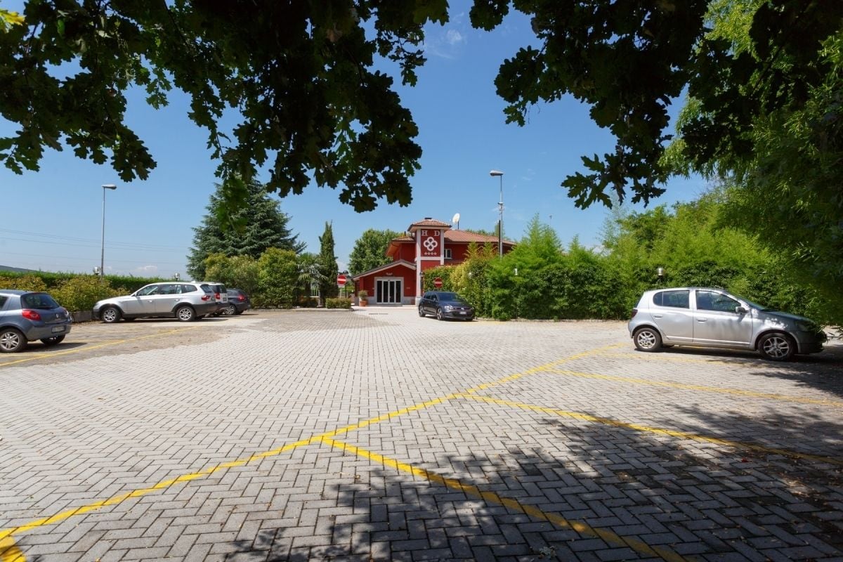 Um espaço de estacionamento com um edifício vermelho ao fundo, rodeado de árvores.