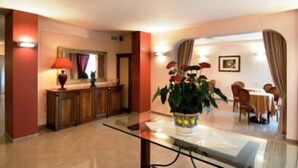 A hotel lobby with a reception desk, a dining area, and a large potted plant. - Daniel (Basiano)