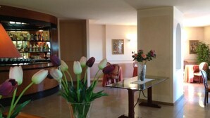 A lobby with a bar area, a glass table with a vase of flowers, and a seating area with chairs. - Daniel (Basiano)