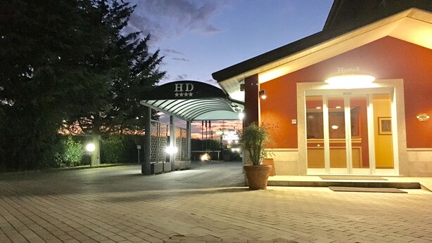 A hotel entrance with a covered walkway, a potted plant, and a sign indicating the hotel name. - Daniel (Basiano)