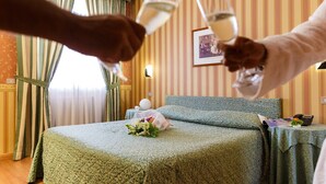 A hotel room with a bed, a bedside table with a lamp, a framed picture on the wall, and a bouquet of flowers on the bed. - Daniel (Basiano)