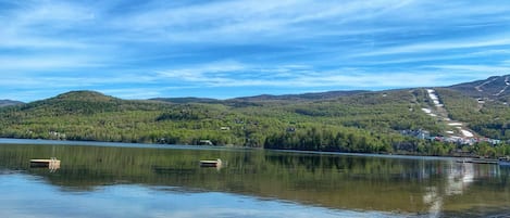A calm lake with clear water reflecting the sky and surrounding landscape. There are wooden docks extending into the lake, and a sandy beach area is visible in the foreground.