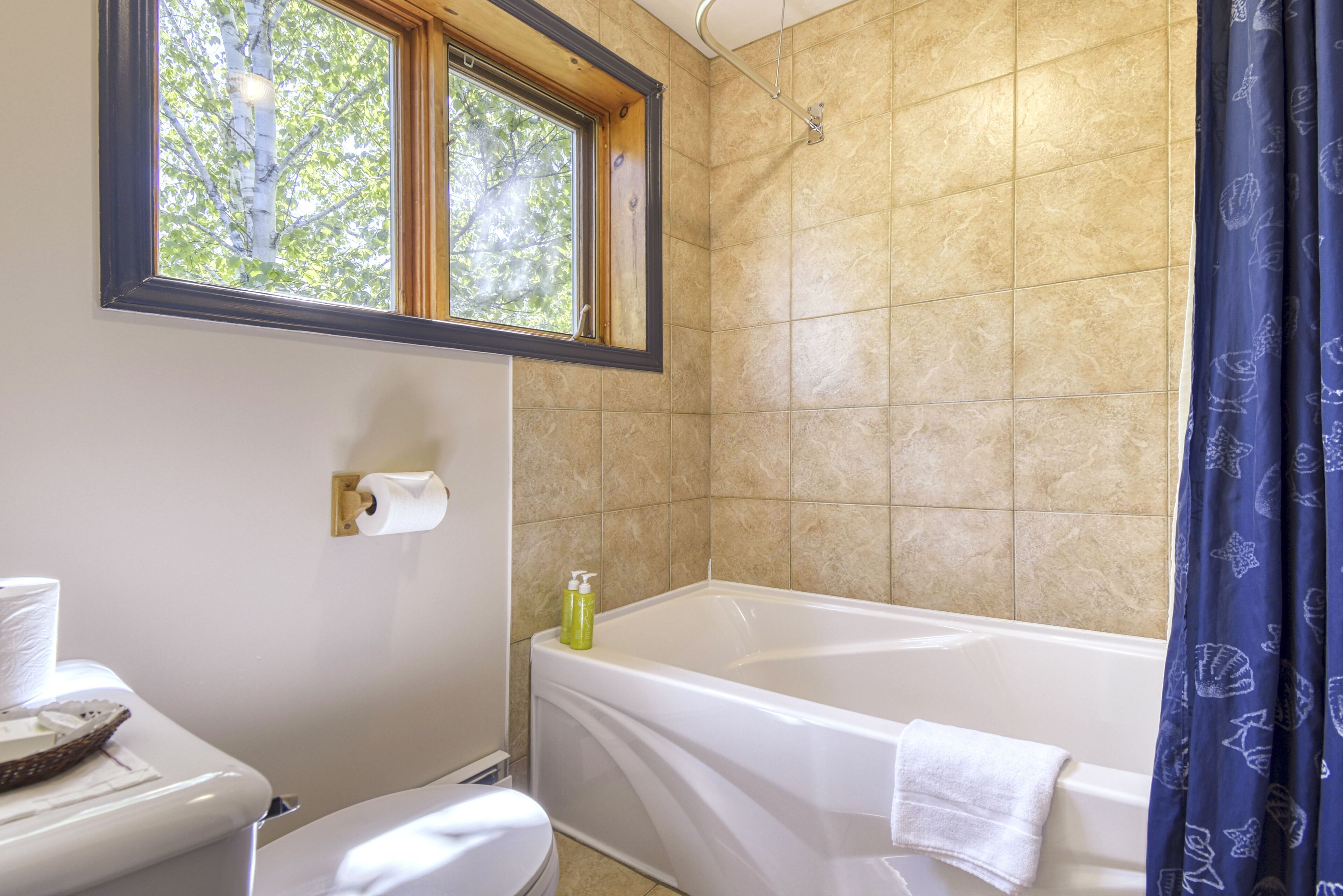 A bathroom with a bathtub, toilet, and window.
