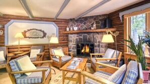 Acogedor interior de cabaña de madera con chimenea de piedra, muebles de estampado escocés y un ventanal grande.