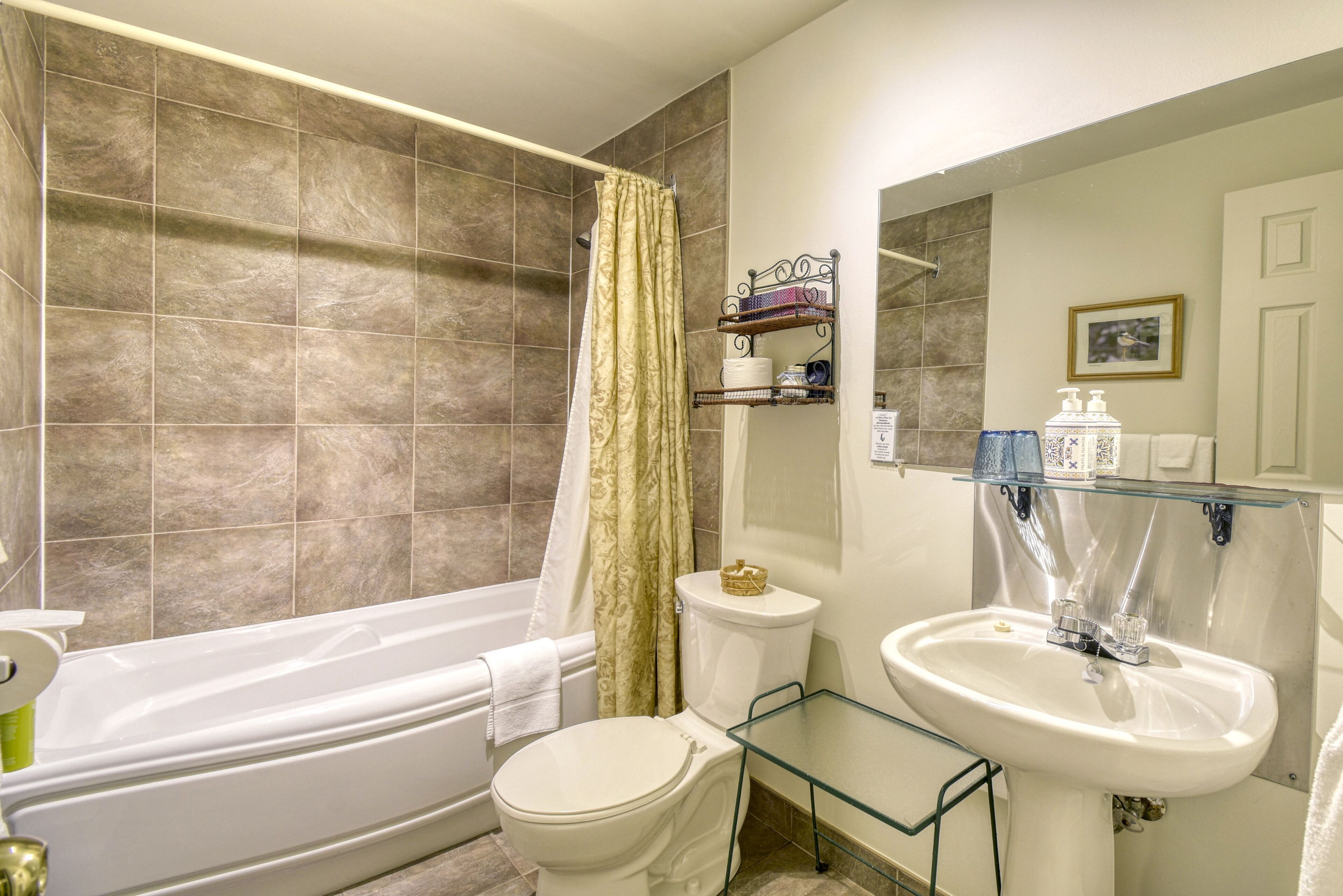 A bathroom with a bathtub, toilet, and glass shelf holding toiletries.