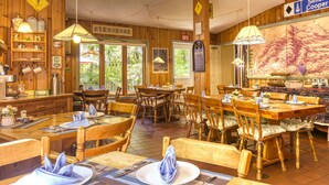Un restaurante con interiores de madera, varias mesas y sillas para comer. Hay lámparas colgantes, un letrero que dice 'Simon Cooper' y una pizarra con el menú.