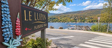 A sign for Le Lupin Auberge B&B with a view of a lake and boats.