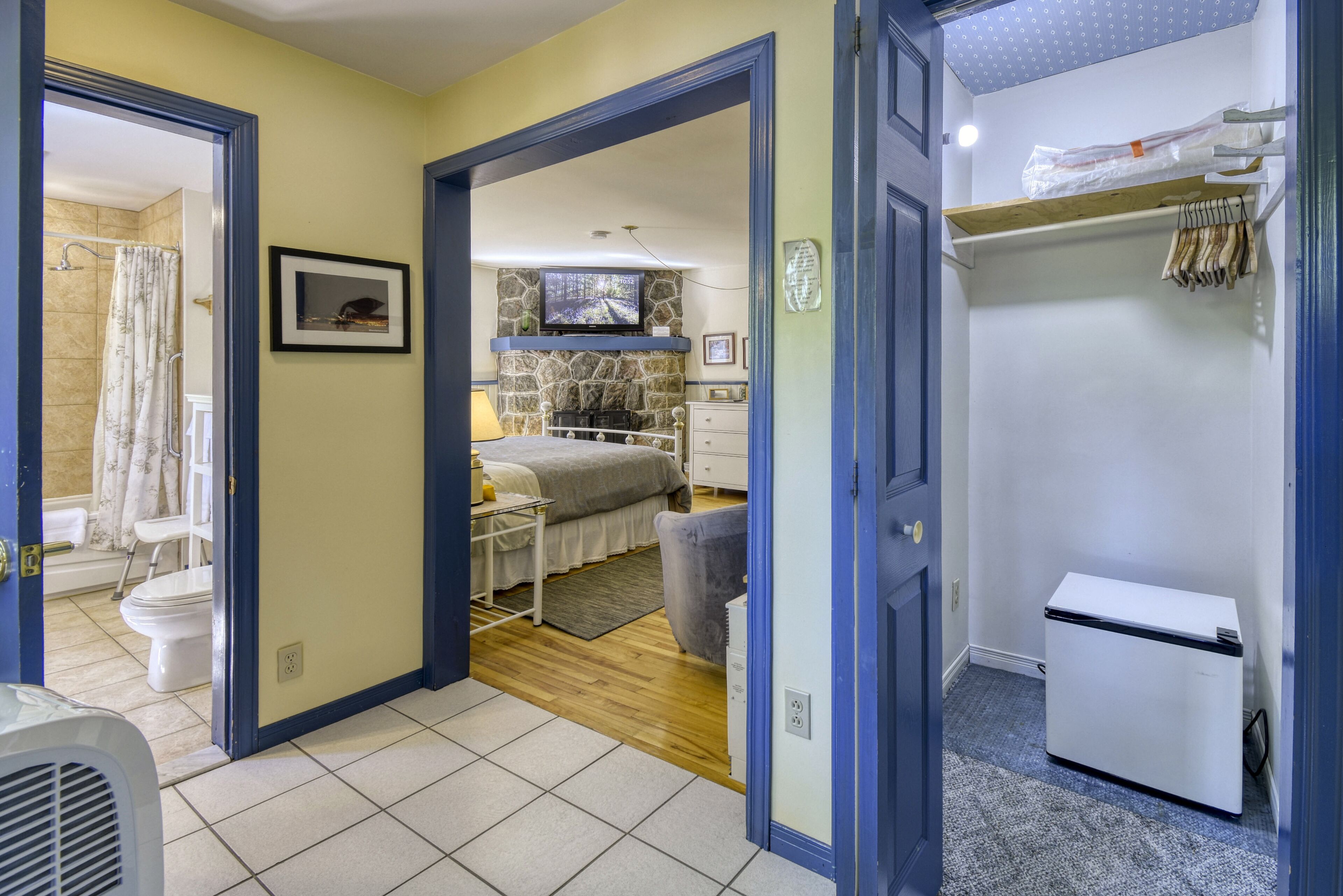 A compact room with a bed, a small refrigerator, and a bathroom with a shower curtain.