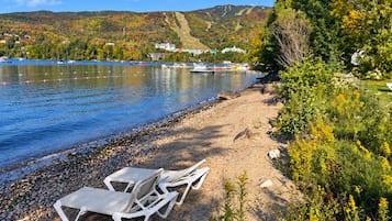 A lakeside view with lounge chairs on the shore, a clear sky, and a hilly landscape in the background.