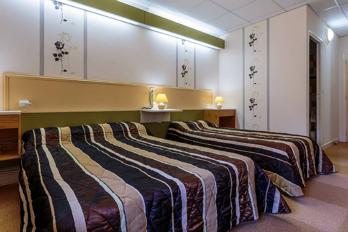 A hotel room with two beds, each with striped bedding, bedside lamps, and floral wall decorations.