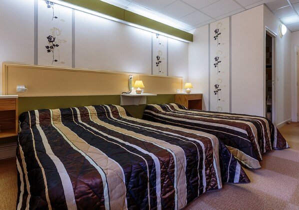 A hotel room with two beds, each with striped bedding, bedside lamps, and floral wall decorations.