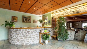 A reception area with a stone counter, wooden ceiling, and potted plants. - Hôtel-Restaurant La Crèche et sa piscine intérieure - Logis Hôtels (La Chomette)