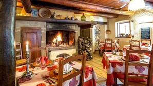 A rustic dining area with a fireplace, wooden beams, and a stone wall. Tables are set with red tablecloths and candles. - Hôtel-Restaurant La Crèche et sa piscine intérieure - Logis Hôtels (La Chomette)