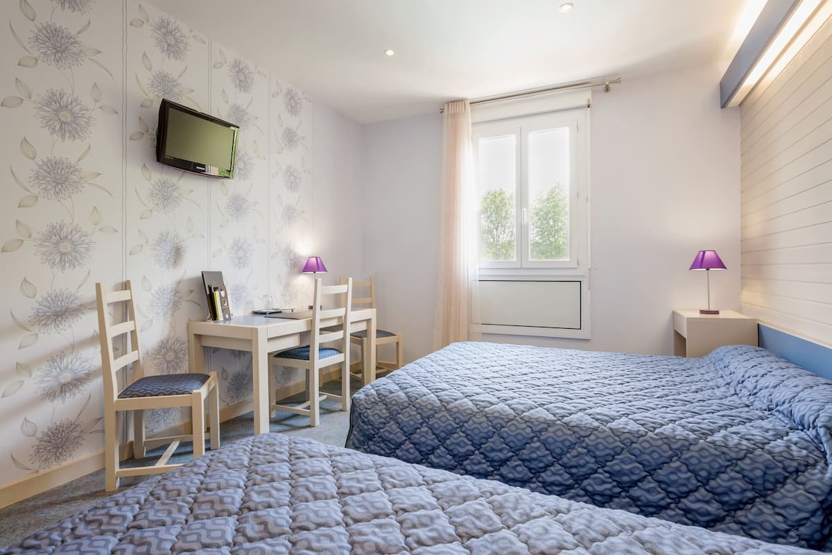 A bedroom with two beds, a desk, chairs, a TV, and a window with curtains.