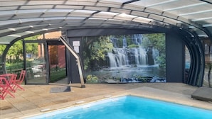 A covered outdoor pool area with a waterfall mural, lounge chairs, and a red chair. - Hôtel-Restaurant La Crèche et sa piscine intérieure - Logis Hôtels (La Chomette)