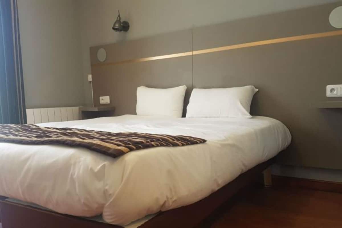 Une chambre d’hôtel moderne, dotée d’un grand lit, d’une table de chevet, d’une lampe et d’un panneau de commande fixé au mur.
