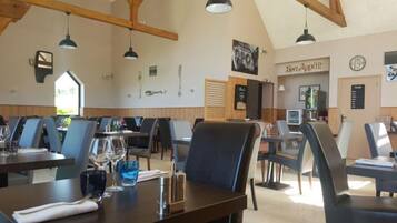 Un restaurant avec de hautes poutres en bois, un éclairage moderne suspendu et un tableau affichant le menu, sur lequel on peut lire « Bon appétit ».