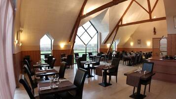 A spacious dining area with high ceilings and large windows, featuring multiple tables and chairs.