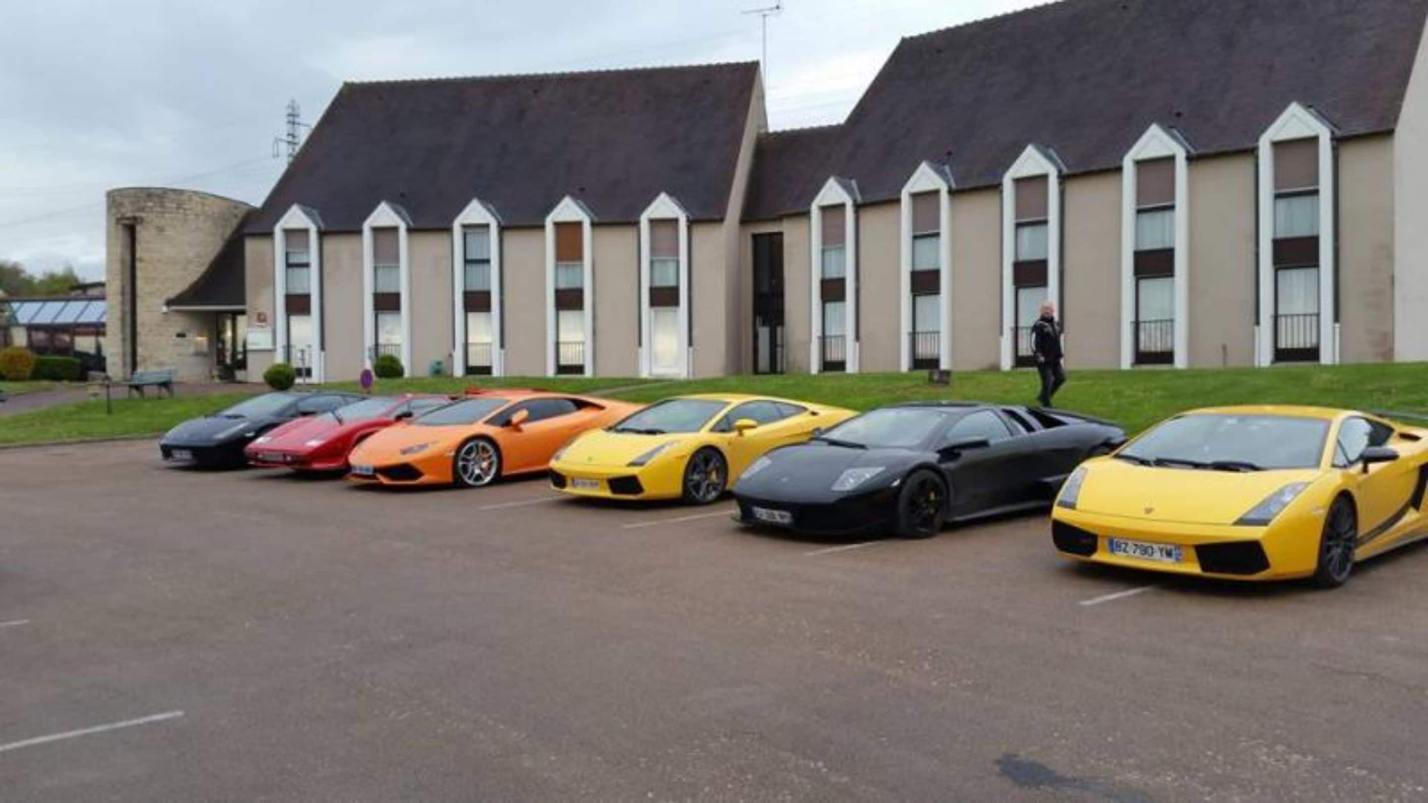 A row of luxury sports cars parked in front of a building with a modern architectural style, featuring a series of windows and a flat roof.