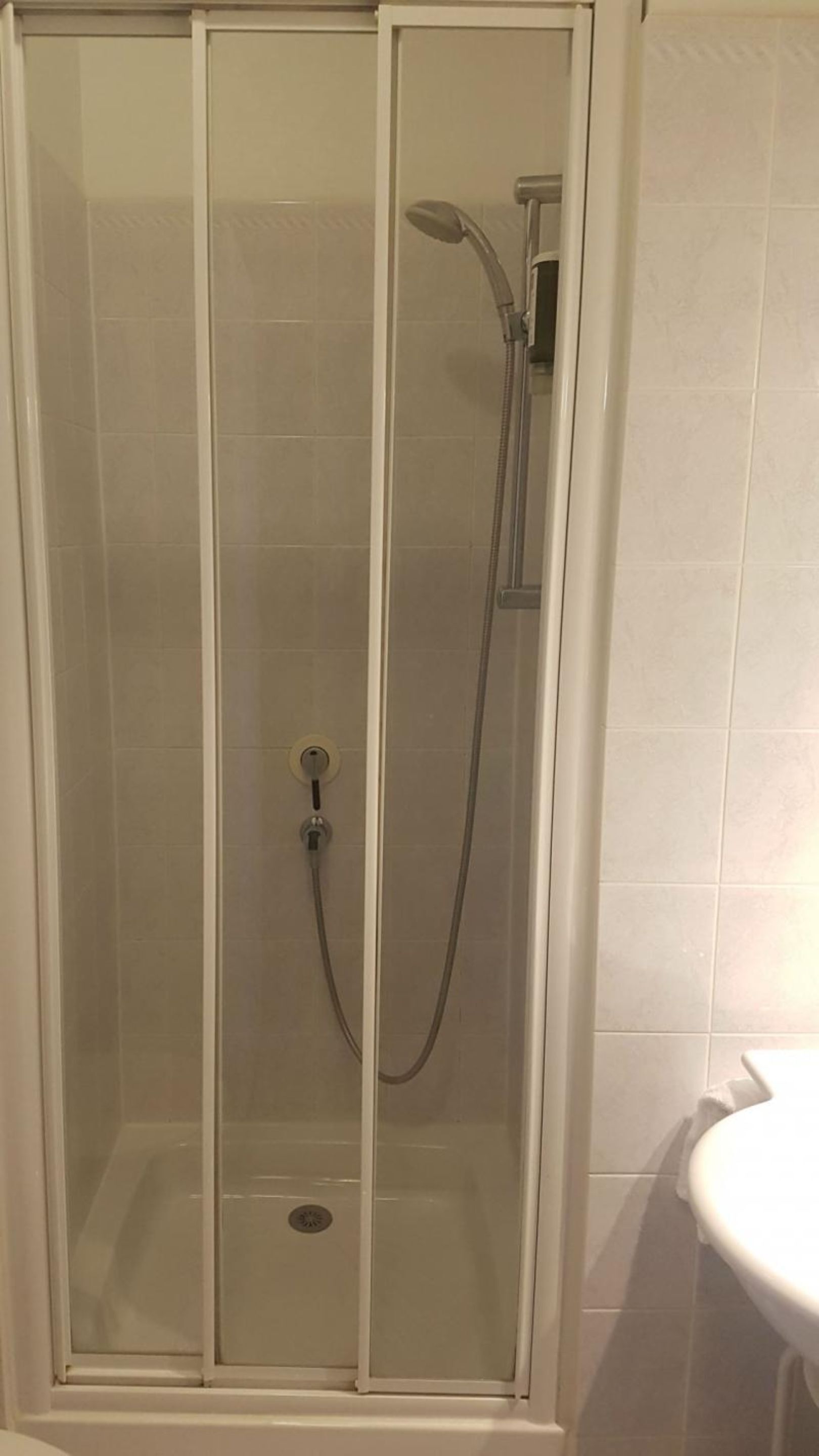 Une cabine de douche fermée par des parois en verre, dotée d’un pommeau de douche à main et d’un robinet mural.
