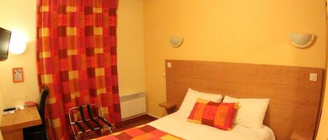 A hotel room with a bed, a desk, a chair, and a TV.