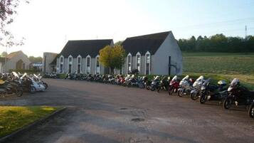 A parking lot with multiple motorcycles lined up in front of a building with a distinct architectural style, including pointed windows and a steeply pitched roof.