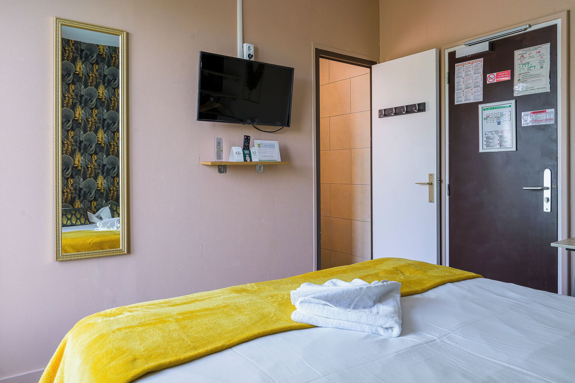 Habitación de hotel con cama, televisión, espejo y puerta con avisos.