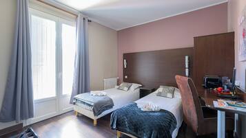 Quarto de hotel com duas camas, uma escrivaninha e uma cadeira.