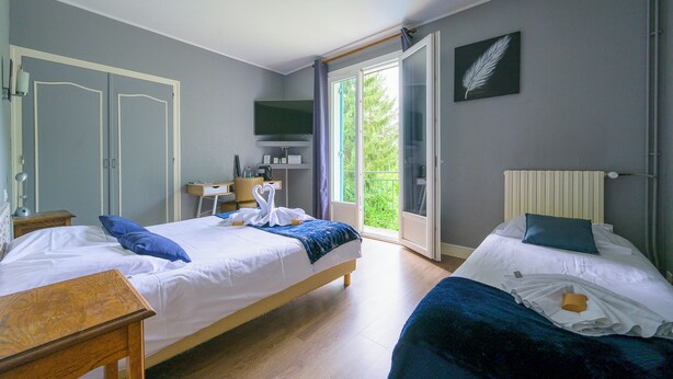 Habitación de hotel con dos camas, un escritorio, televisión y balcón con vistas a zonas verdes.