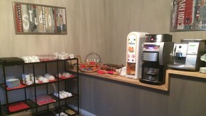 Una estación de café con una cafetera, una estación de té y una repisa con tazas y platos.