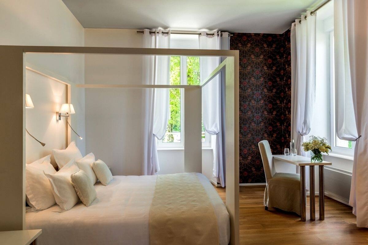 Un dormitorio con una cama con dosel, una mesita con un jarrón de flores y una silla.