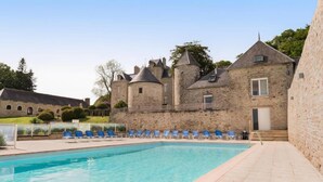 Un bâtiment en pierre doté d’une piscine et de chaises longues bleues.