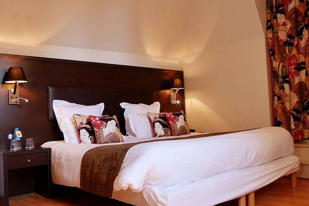 Habitación de hotel con una cama grande, dos mesitas de noche, lámparas de pared y una cortina de estilo japonés tradicional.